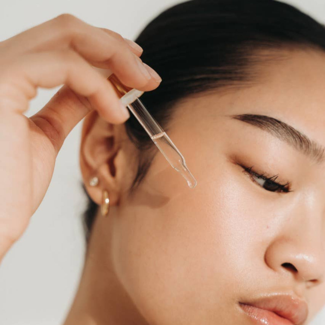 Person applying a dropper of skincare product to their face.