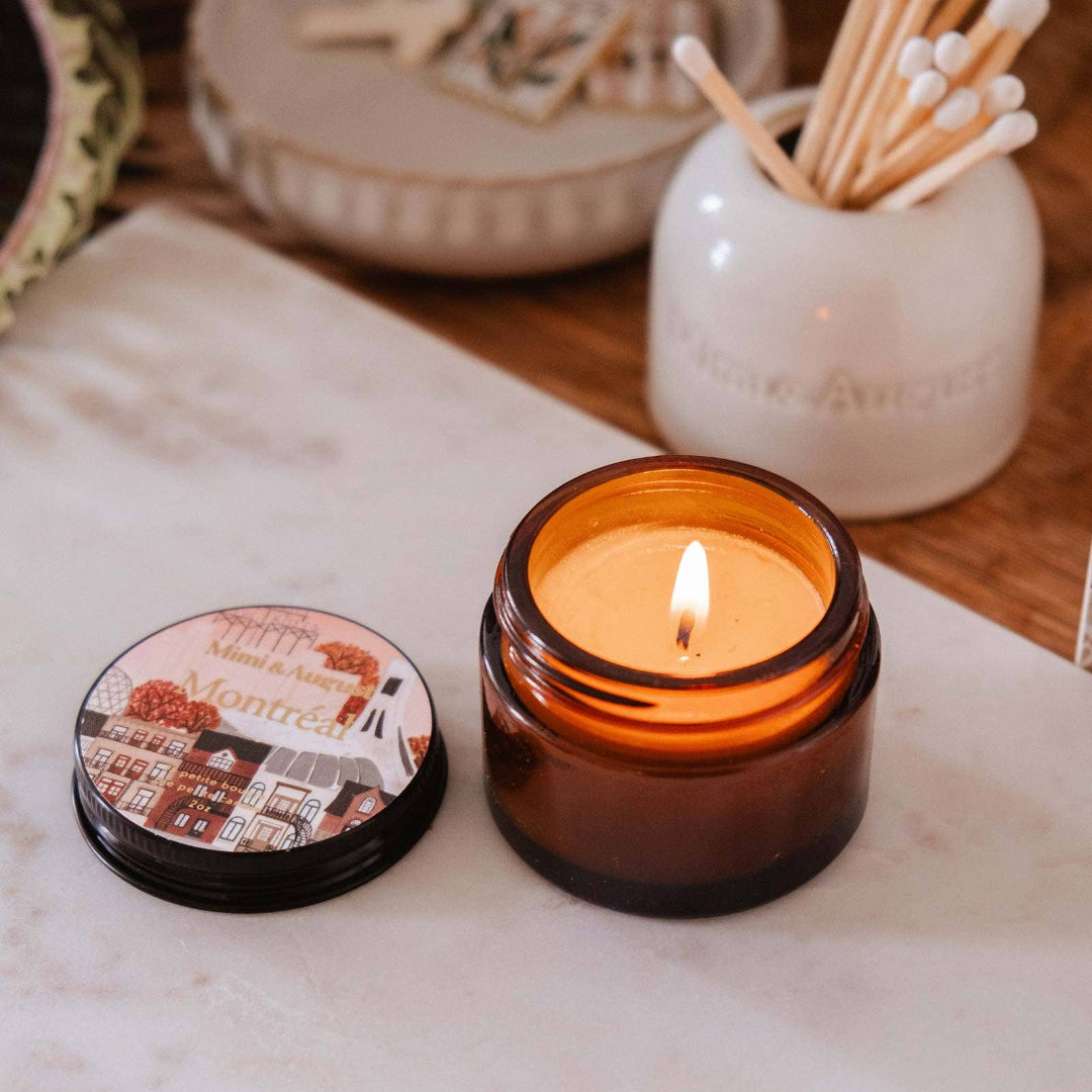 Candle in an amber jar with a lit wick, surrounded by decorative items on a wooden surface.