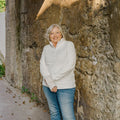 Woman in a white hoodie and blue jeans standing against a stone wall.