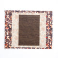 Decorative quilt with floral pattern border and brown square in center on white background