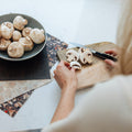 Person cutting mushrooms on a wooden cutting board with a bowl of mushrooms nearby.