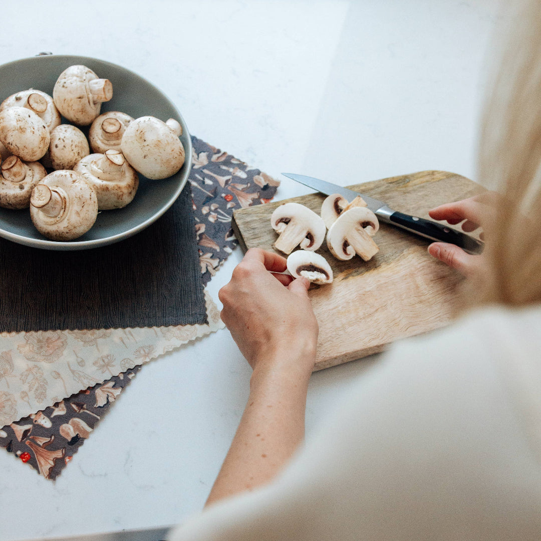 Person cutting mushrooms on a wooden cutting board with a bowl of mushrooms nearby.