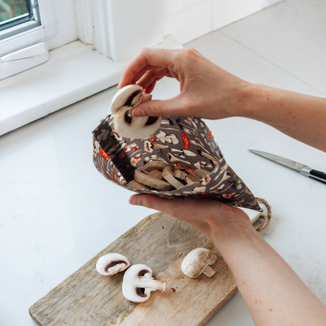 Person holding a small bag with mushrooms on a wooden cutting board.