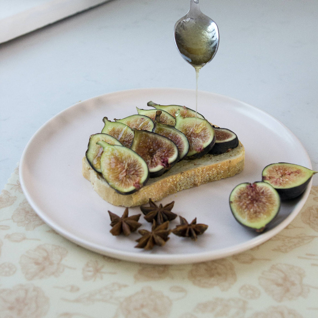 Person drizzling honey over figs on toast with a spoon on a white plate.