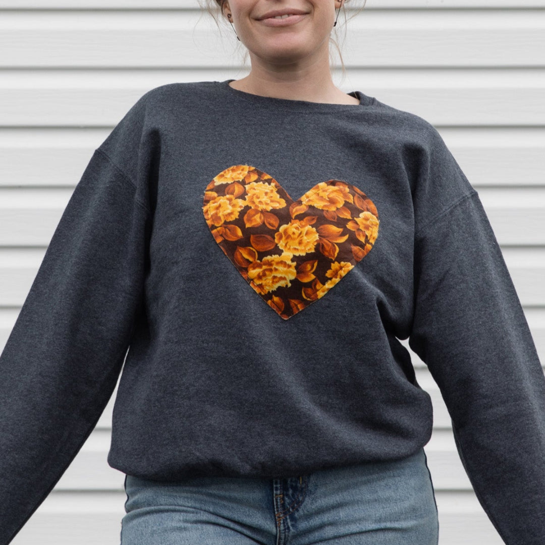 Person wearing a dark gray sweatshirt with a floral heart design, standing against a light-colored wall.