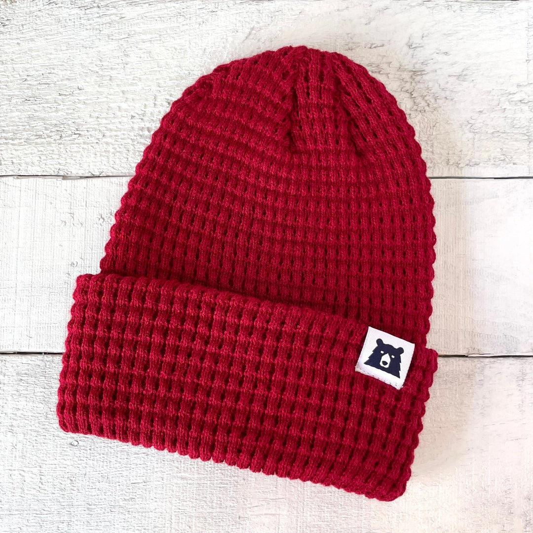Red knit beanie with a small logo on a light wooden surface