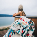 The Nibi Reversible Blanket by Mini Tipi, featuring bold Indigenous-inspired geometric patterns in teal, red, brown, and white, piled next to a hottub. This reversible and stylish blanket is available in Ottawa, Ontario, Canada.