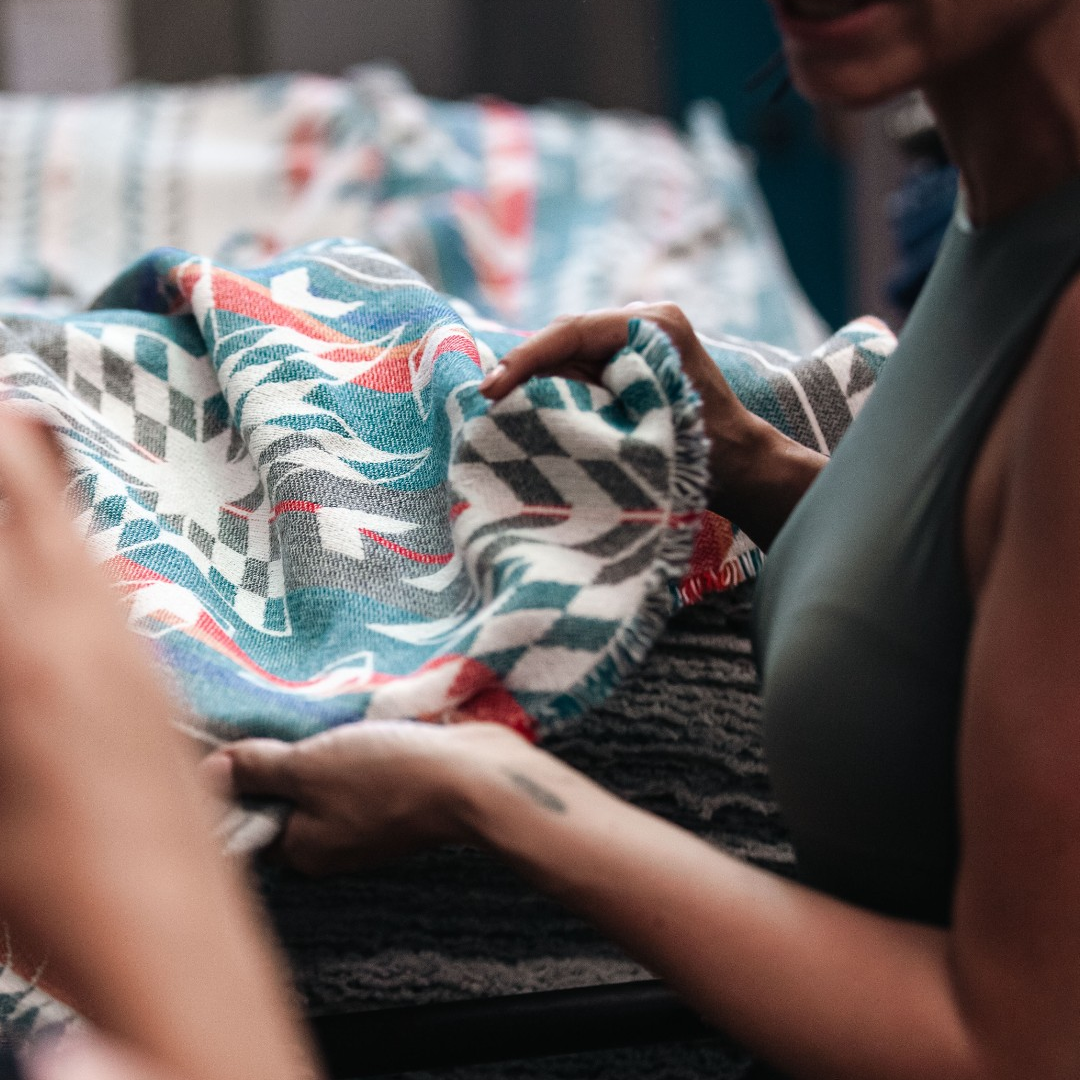 The Nibi Reversible Blanket by Mini Tipi, featuring bold Indigenous-inspired geometric patterns in teal, red, brown, and white, in the manufacturing process. This reversible and stylish blanket is available in Ottawa, Ontario, Canada.