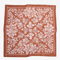 A terracotta-colored bandana with a floral pattern. The pattern features white flowers with pink centers and green leaves. The border of the bandana has a decorative, repeating pattern.