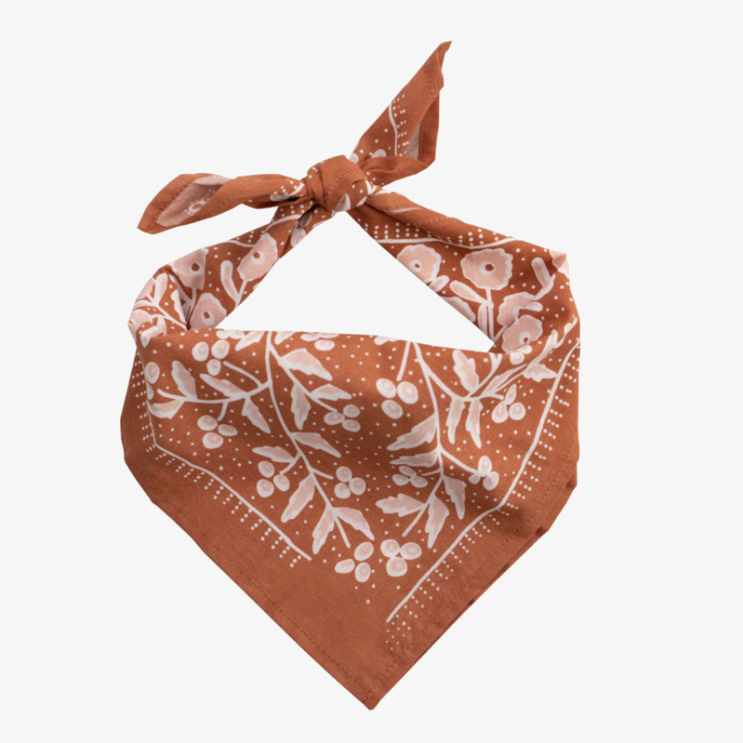 A terracotta-colored bandana with a floral pattern. The pattern features white flowers with pink centers and green leaves. The border of the bandana has a decorative, repeating pattern.
