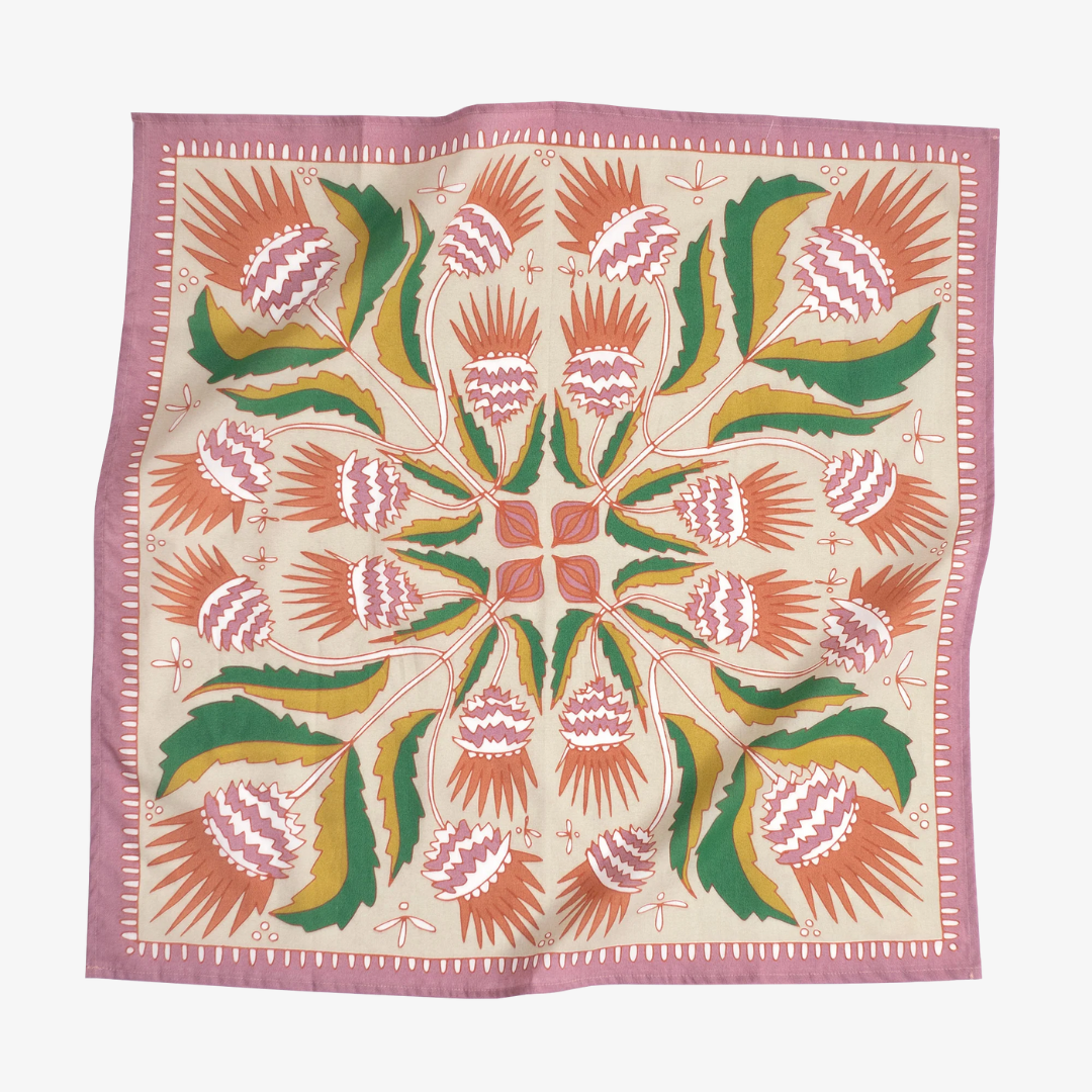 A pink bandana with a floral pattern. The pattern features pink and orange flowers with green leaves on a cream background. The border of the bandana is pink with a decorative pattern.