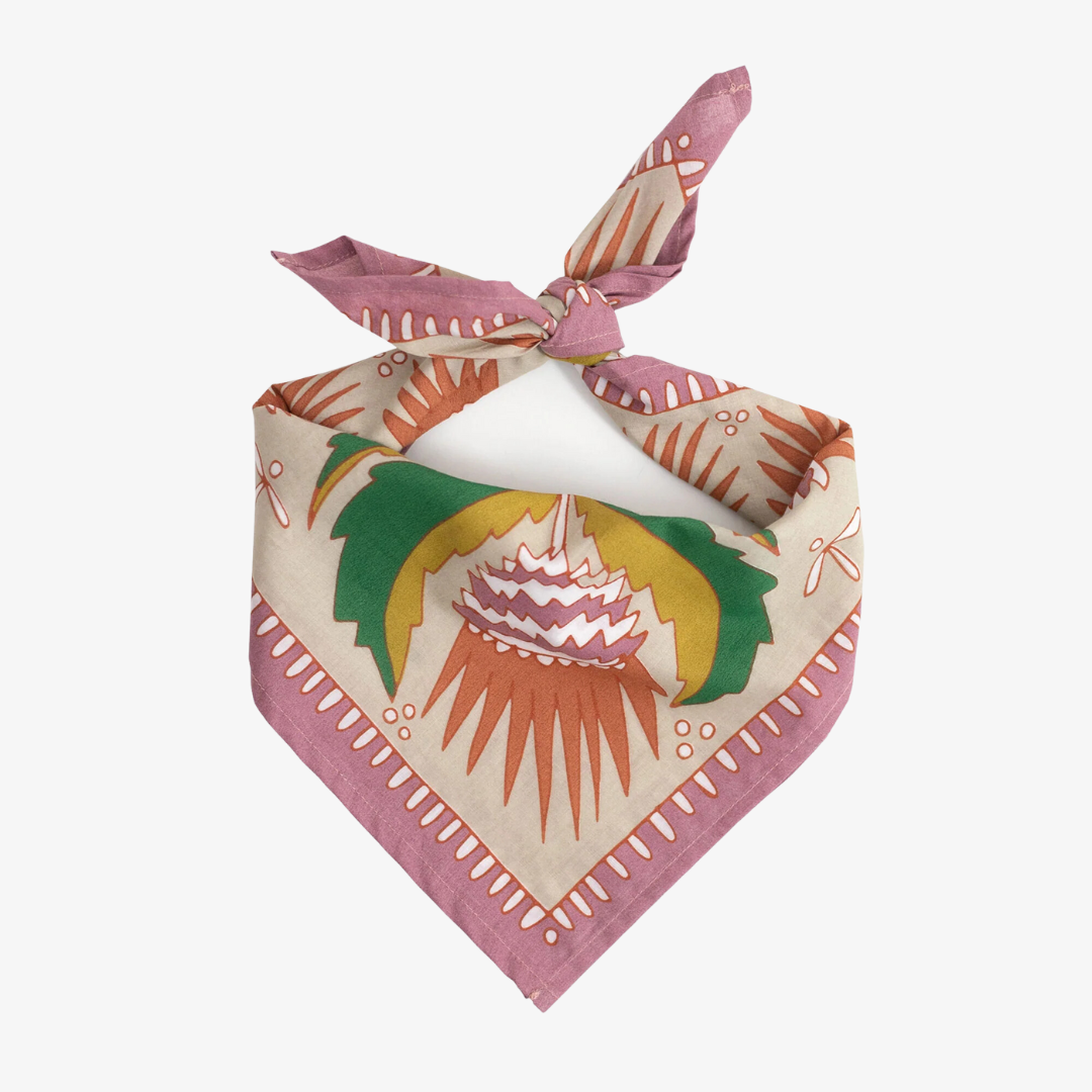 A pink bandana with a floral pattern. The pattern features pink and orange flowers with green leaves on a cream background. The border of the bandana is pink with a decorative pattern.