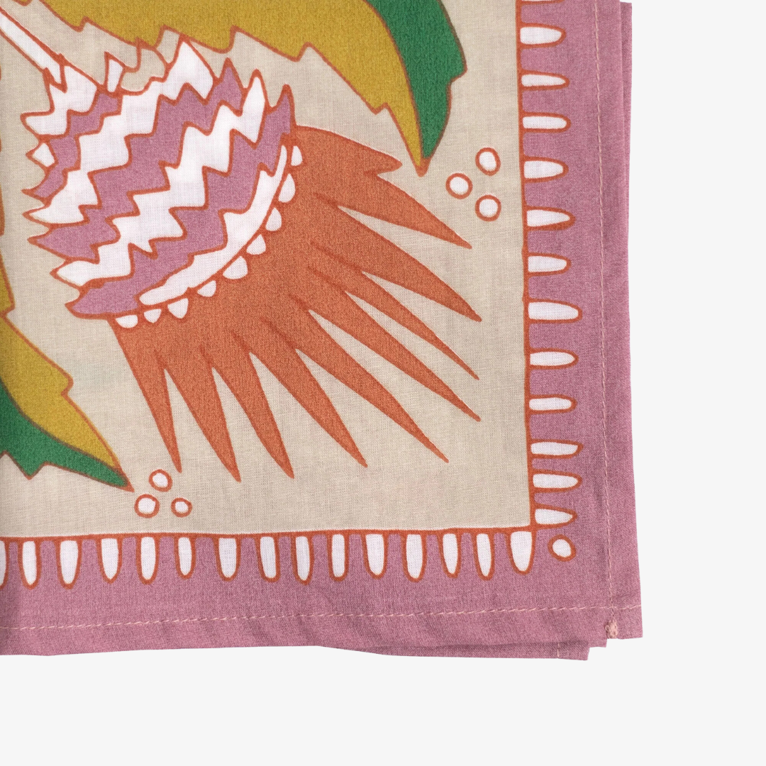 A pink bandana with a floral pattern. The pattern features pink and orange flowers with green leaves on a cream background. The border of the bandana is pink with a decorative pattern.