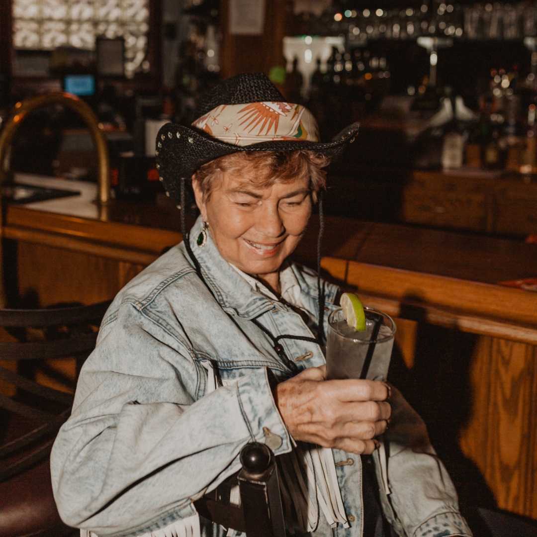A pink bandana with a floral pattern. The pattern features pink and orange flowers with green leaves on a cream background. The border of the bandana is pink with a decorative pattern.