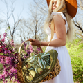 Woman holding a floral-patterned bag with a white dress and brown hat in a park setting