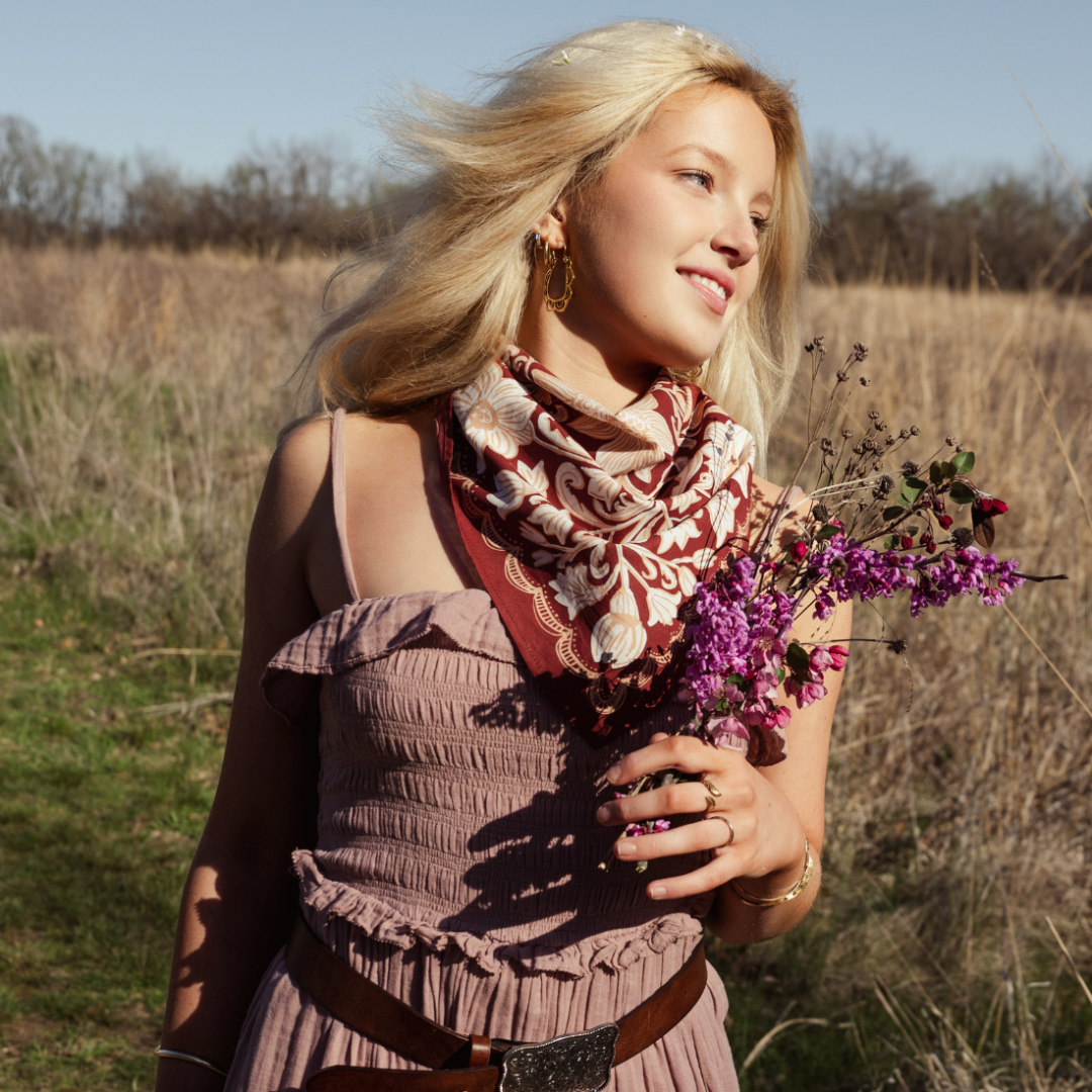 Woman holding flowers in a field with a scarf around her neck
