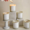 A collection of North + Rose candles with wood wicks and a hand lighting them with a match.