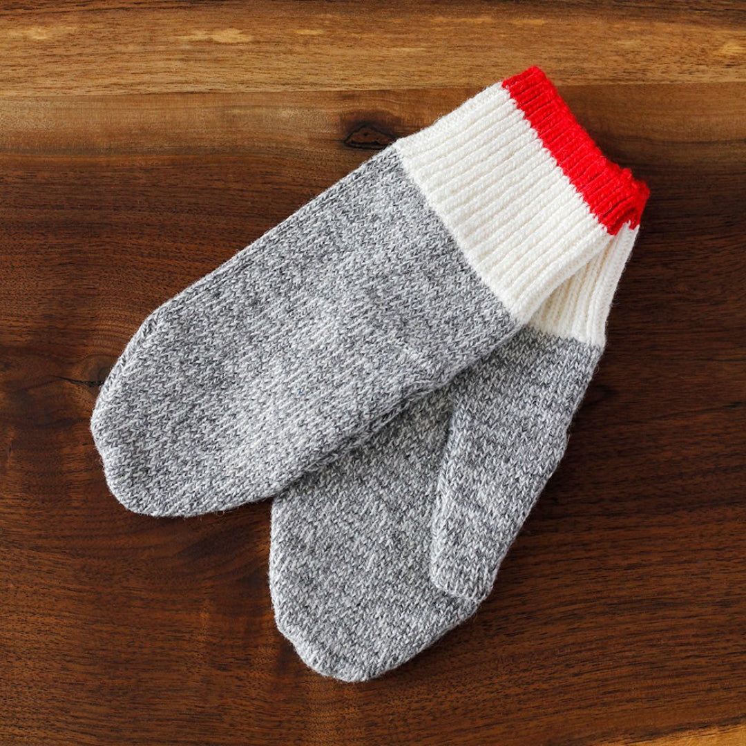 Gray and white mittens with red cuff on a wooden surface