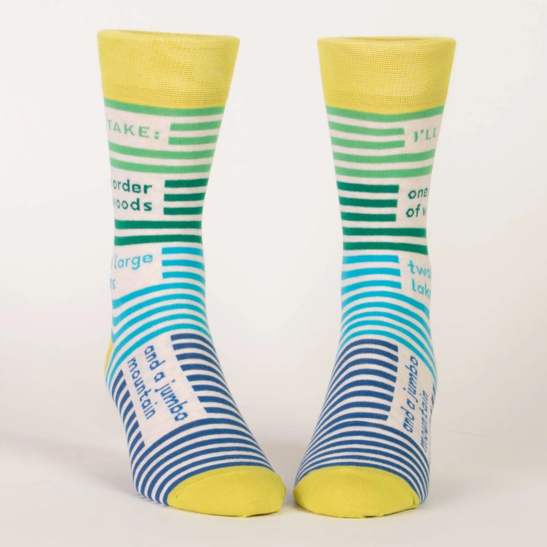 pair of men's crew socks with a vibrant stripe pattern. One sock features wide horizontal green and blue stripes, while the other has blue and white stripes on the foot and green and white stripes on the calf. Text on the socks reads "I'LL TAKE: one order of woods two large lakes and a jumbo mountain."