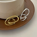 A set of silver and gold-plated geometric open statement twist rings, featuring unique, flowing designs, displayed side-by-side on a light-colored surface. These are modern and bold rings, available in Ottawa, Ontario, Canada.