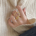 A gold-plated geometric open statement twist ring, featuring a unique, flowing design, worn on a person's finger against a light-colored sweater. This is a modern and bold ring, available in Ottawa, Ontario, Canada.