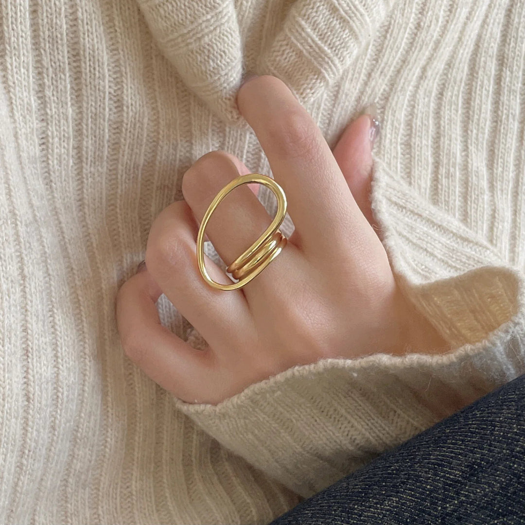 A gold-plated geometric open statement twist ring, featuring a unique, flowing design, worn on a person's finger against a light-colored sweater. This is a modern and bold ring, available in Ottawa, Ontario, Canada.