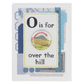 A birthday card with a vintage, collage-like design. It features a large white flashcard with a black capital "O" followed by "is for" and "over the hill" in black text. A glossy round button with a landscape illustration of green hills and a red arrow pointing downwards is centered on the flashcard. The background of the card includes faded map details, ruler markings, and decorative blue and grey patterns.