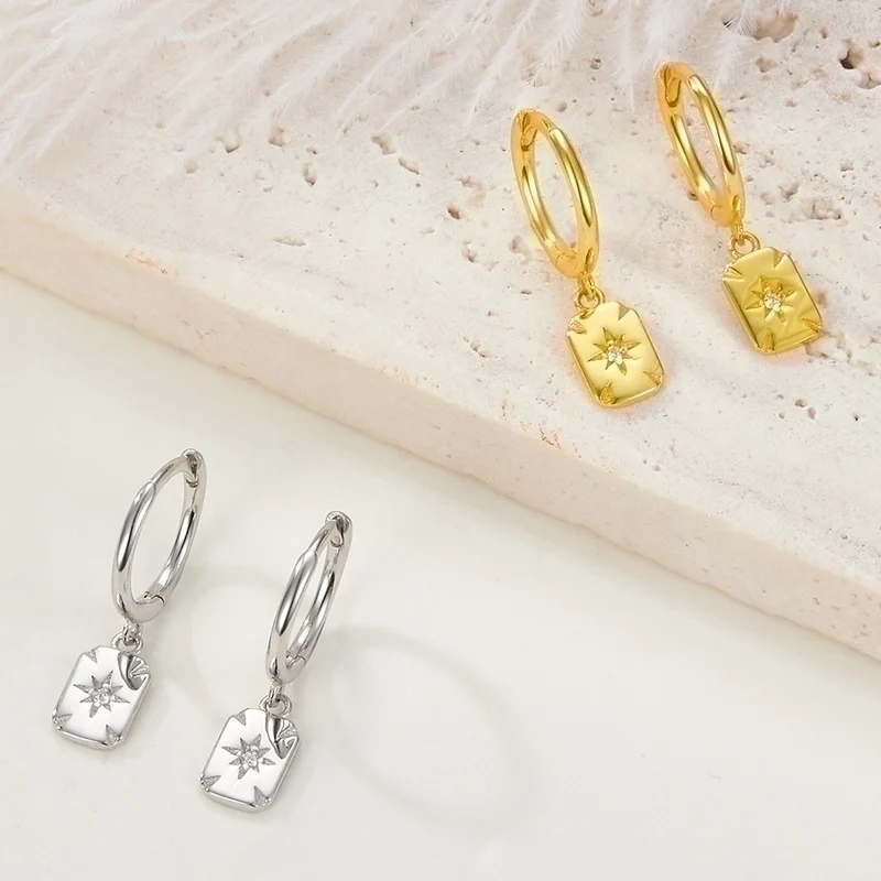 Silver and gold plated starburst square dangle hoop earrings, potentially Bohomoon style, featuring small hoops with dangling square charms, each with an etched starburst design and a central sparkling crystal. These modern earrings are available in Ottawa, Ontario, Canada.