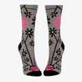 A pair of women's crew socks with a grey background and a pattern of black and white flowers on branches. One sock has text in bright pink that reads "MOST LIKELY TO SAY IT TO YOUR FACE".