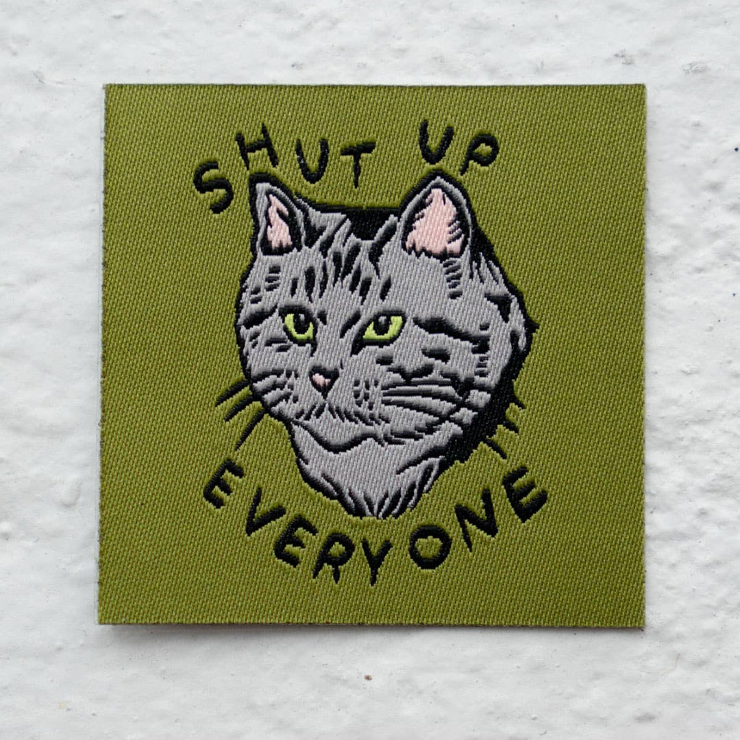 Embroidered patch with a cat illustration and text 'SHUT UP EVERYONE' on a green background.
