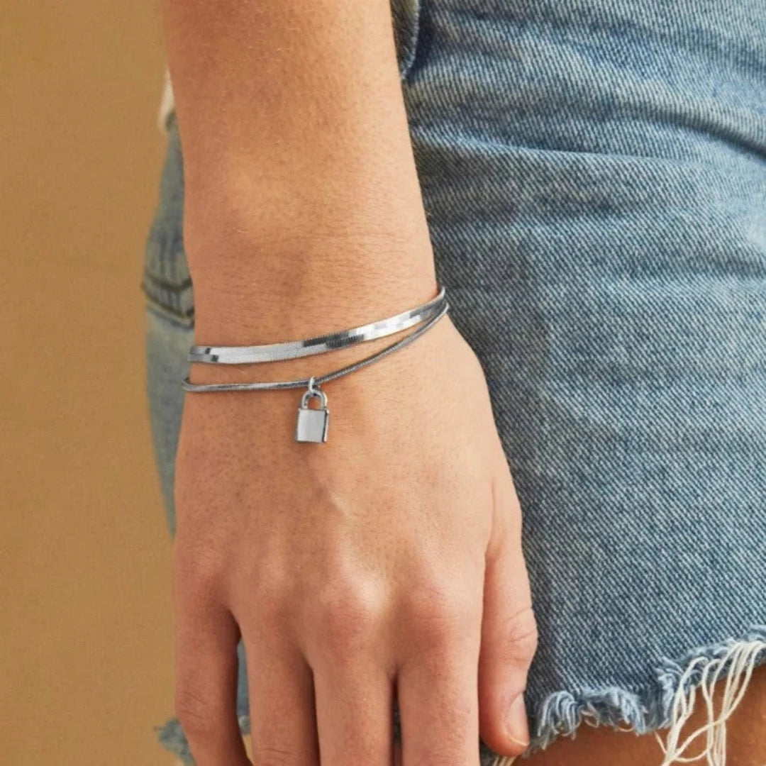 A silver layered bracelet with a small padlock charm. The bracelet has two chains of different widths, and the padlock charm hangs from the thinner chain.