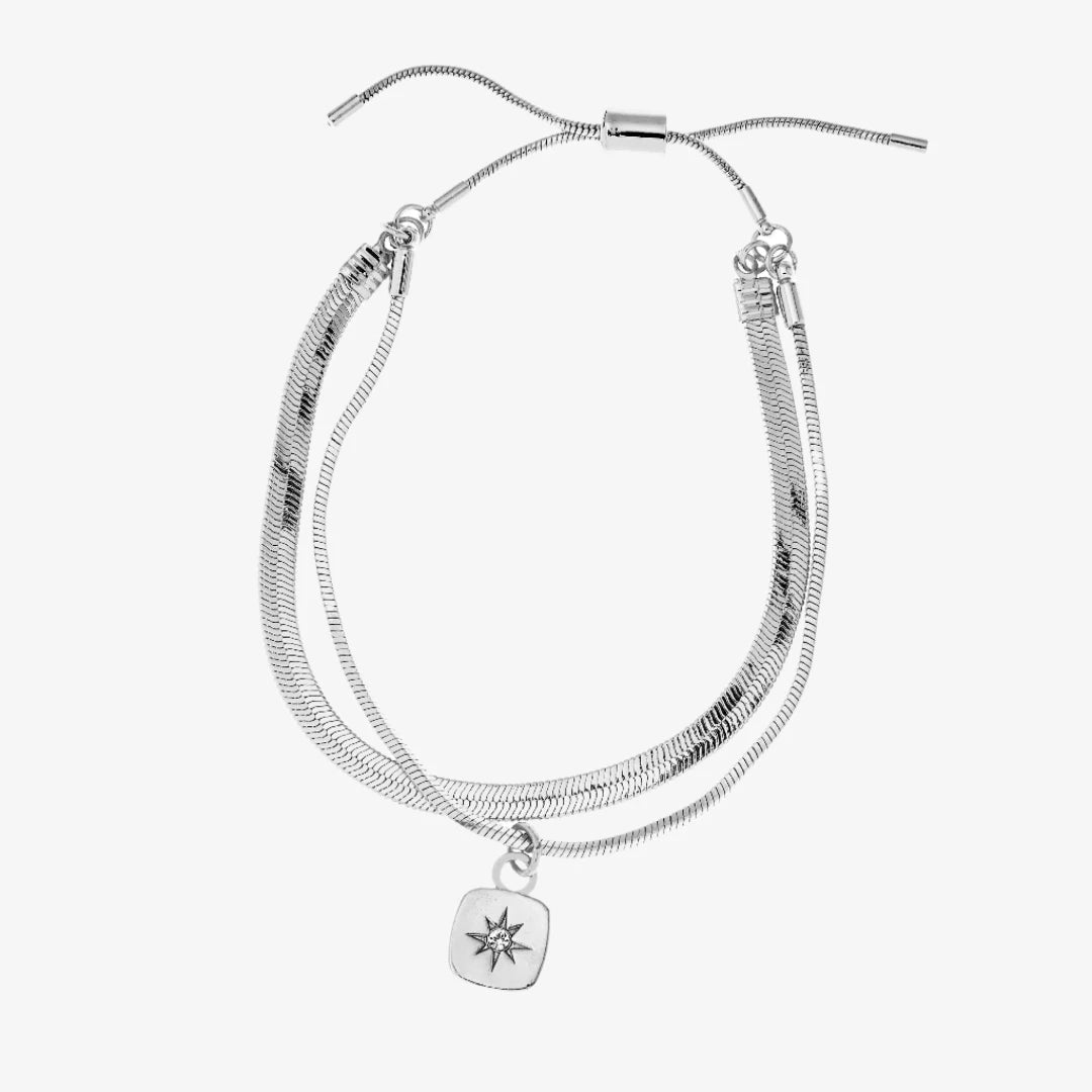 A set of two silver bracelets, one layered over the other, with a star charm hanging from the bottom. The bracelets are displayed on a pink card with the brand name "Foxy Originals."