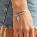 A set of two silver bracelets, one layered over the other, with a star charm hanging from the bottom. The bracelets are displayed on a pink card with the brand name "Foxy Originals."