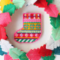 a colorful plastic canvas Christmas stocking ornament. The stocking is pink, yellow, blue, and green with white accents and colorful bead embellishments.