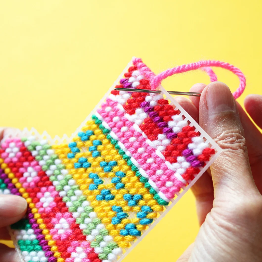 a colorful plastic canvas Christmas stocking ornament. The stocking is pink, yellow, blue, and green with white accents and colorful bead embellishments.