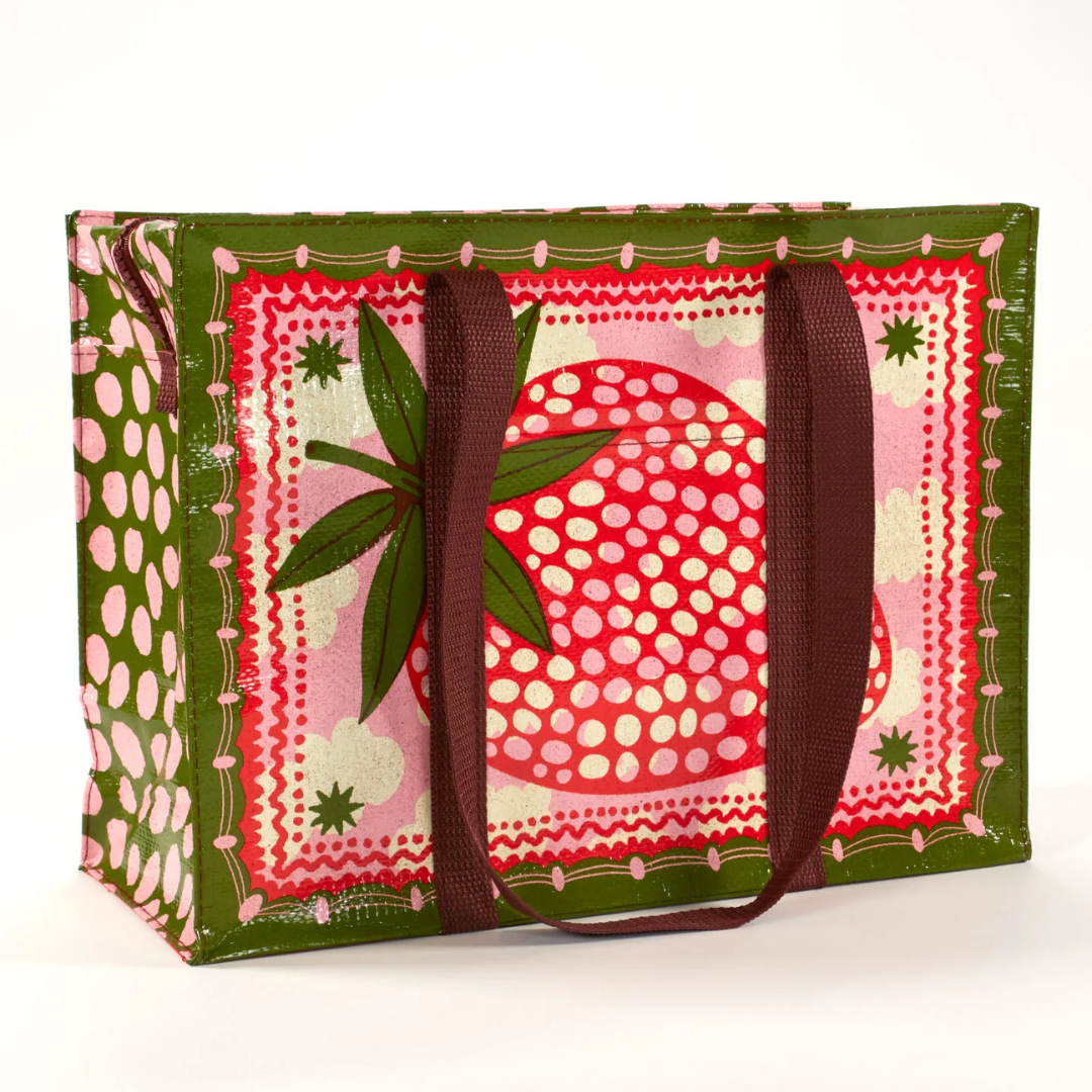 A reusable tote bag with a playful strawberry design. The bag is olive green with brown handles. It features a large pink strawberry in the center, surrounded by white clouds, stars, and pink polka dots. The strawberry has detailed leaves and seeds.