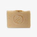 A rectangular bar of soap with a light beige color. There is a circular logo embossed on the center of the soap.