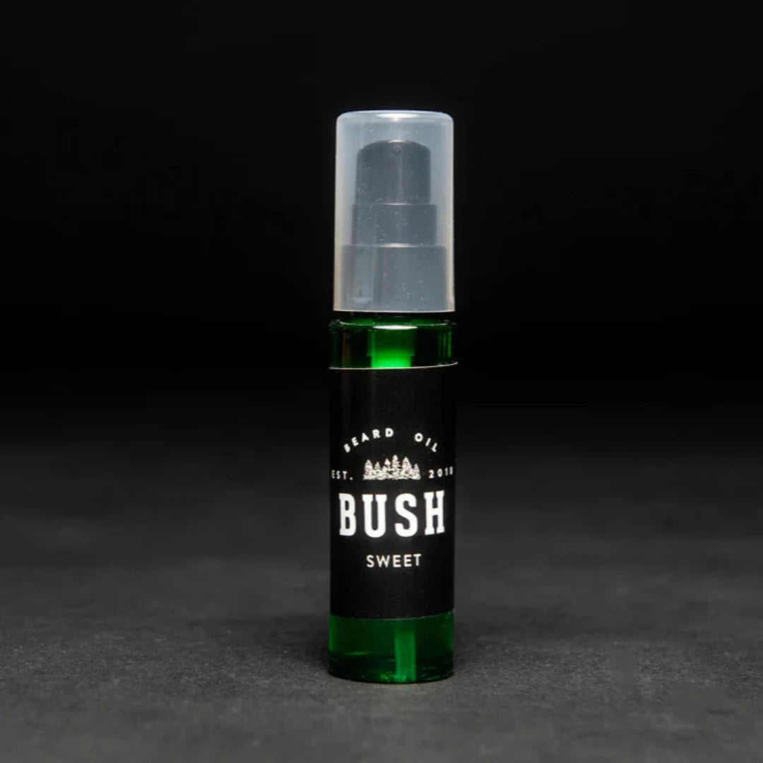 A dark green glass bottle with a black pump dispenser. The bottle is labeled "BUSH" and "SWEET BEARD OIL." The background is black.