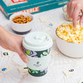 Hand holding a coffee cup with a floral design, surrounded by snacks and a board game.