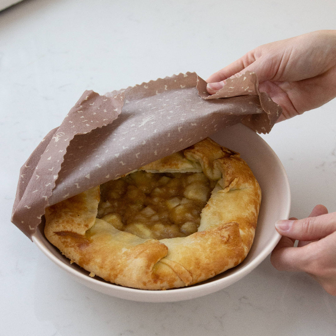 Person covering a baked dish with a brown paper towel on a white surface