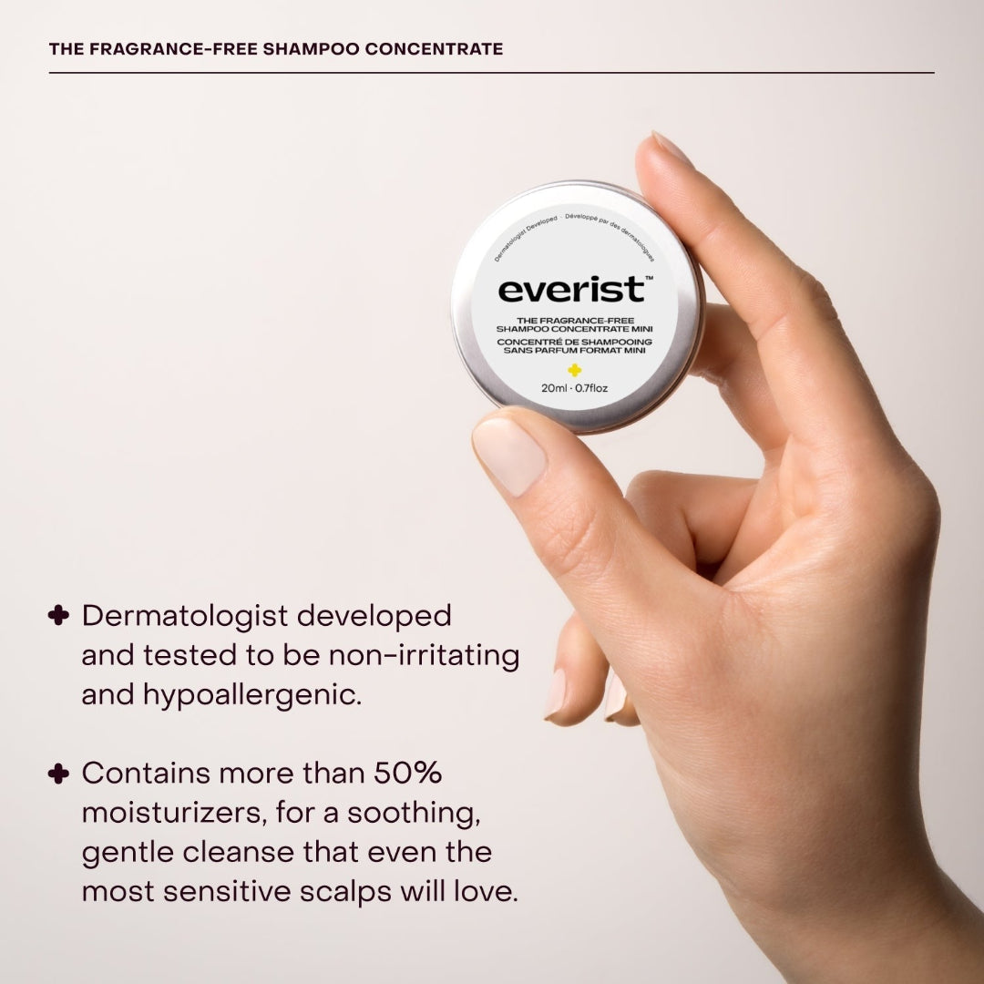 A small, open, silver metal tin of Everist's "The Fragrance-Free Shampoo Concentrate Mini," revealing a white, concentrated product inside. The tin's lid is propped against the base, with text indicating it is dermatologist-developed and contains 20ml of product.