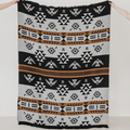 The Thunderbird Reversible Eco-Friendly Blanket by Mini Tipi, featuring bold Indigenous-inspired Thunderbird and geometric patterns in black, grey, and brown, held up by two hands. This sustainable and culturally significant blanket is available in Ottawa, Ontario, Canada.