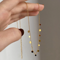 A delicate gold-toned necklace featuring a fine chain with tiny, scattered disc or coin charms, held by a person's hand. This minimalist necklace is available in Ottawa, Ontario, Canada.