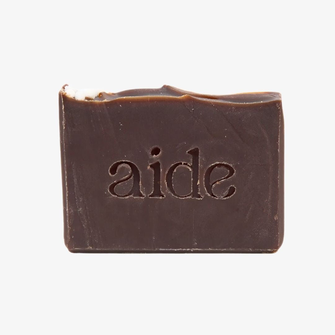 Bar of dark soap with 'aide' embossed on a white background