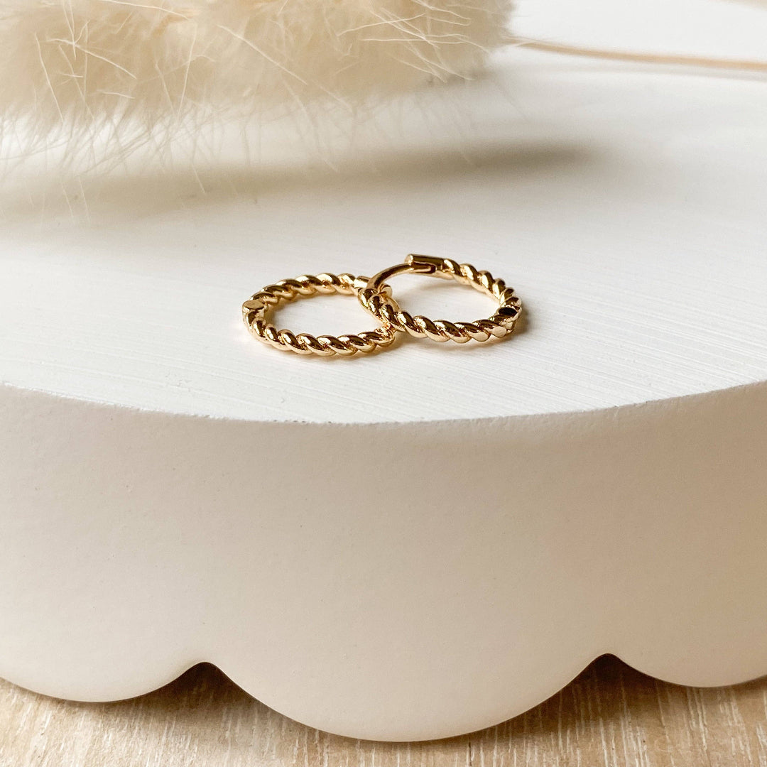 Two gold hoop earrings on a white scalloped edge surface.