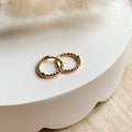 Gold hoop earrings on a white dish with a light wooden background