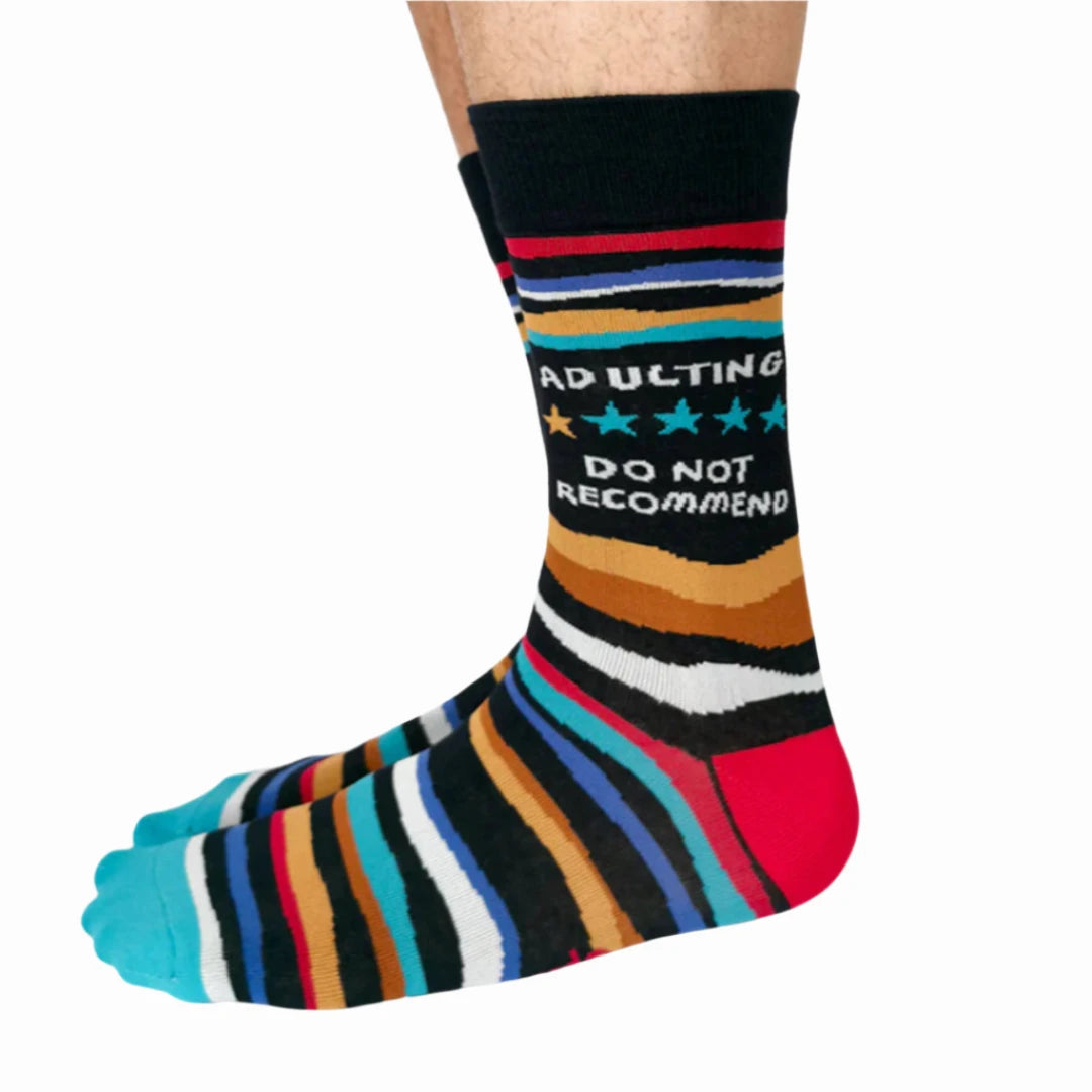 A pair of crew socks with a humorous message. The socks are mostly black with colorful stripes. The text "Adulting" is printed at the top, followed by a star rating of three stars and the phrase "Do Not Recommend."