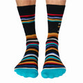 A pair of crew socks with a humorous message. The socks are mostly black with colorful stripes. The text "Adulting" is printed at the top, followed by a star rating of three stars and the phrase "Do Not Recommend."