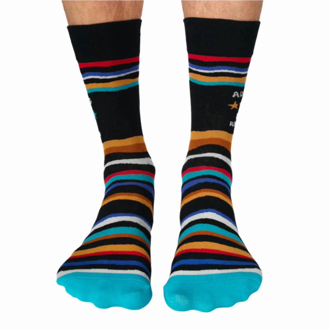 A pair of crew socks with a humorous message. The socks are mostly black with colorful stripes. The text "Adulting" is printed at the top, followed by a star rating of three stars and the phrase "Do Not Recommend."