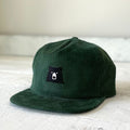 Green corduroy cap with a bear emblem on a light wooden surface